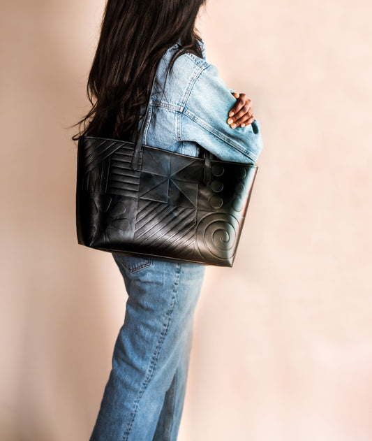 Black leather tote bag featuring Afro-modern Adire motifs, symbolizing cultural heritage and contemporary elegance. Crafted from full-grain Italian leather with vibrant Adire fabric lining. Choose from three colorful variations. Egba Ake
